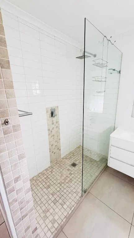 Modern walk-in shower with frameless glass enclosure and mosaic tile flooring