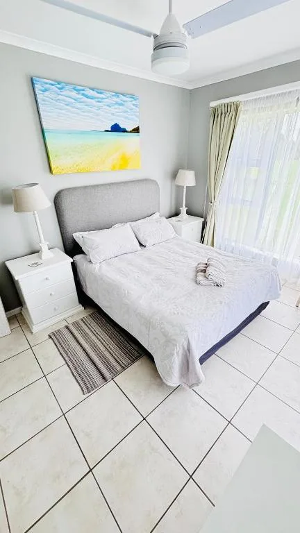 Bright bedroom with queen bed, gray headboard, beach artwork, ceiling fan