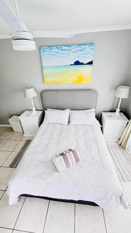 Bright bedroom with queen bed, grey headboard, and beach artwork above