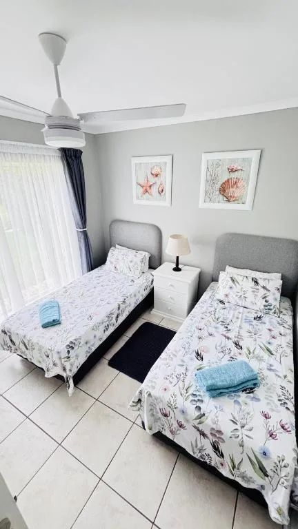 Twin bedroom with floral bedding, ceiling fan, and coastal-themed wall art