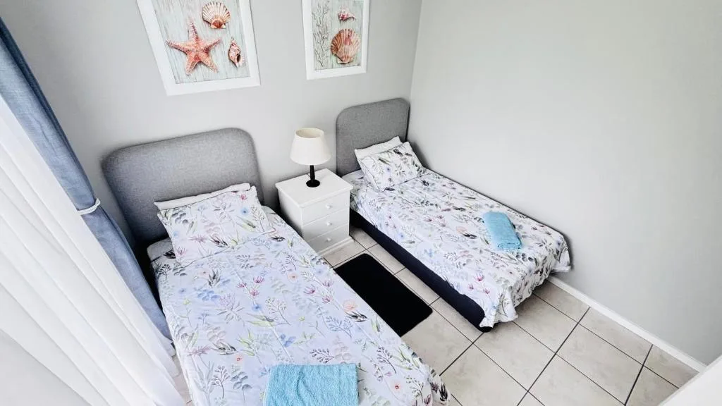 Twin bedroom with floral bedding, grey headboards, coastal decor artwork