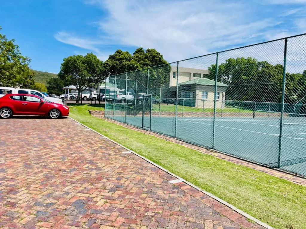Tennis court and driveway with red car parked near white modern apartment building