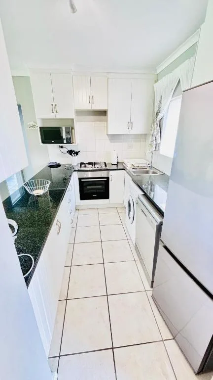 Bright white galley kitchen with gas stove, dishwasher, and granite countertops