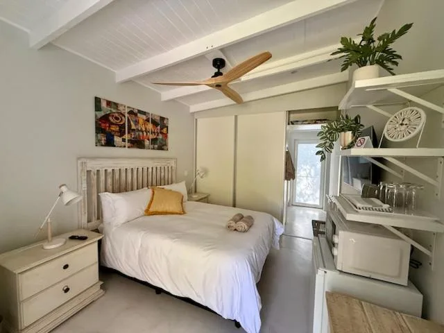 Bright bedroom with white bed, wooden ceiling fan, and open shelving