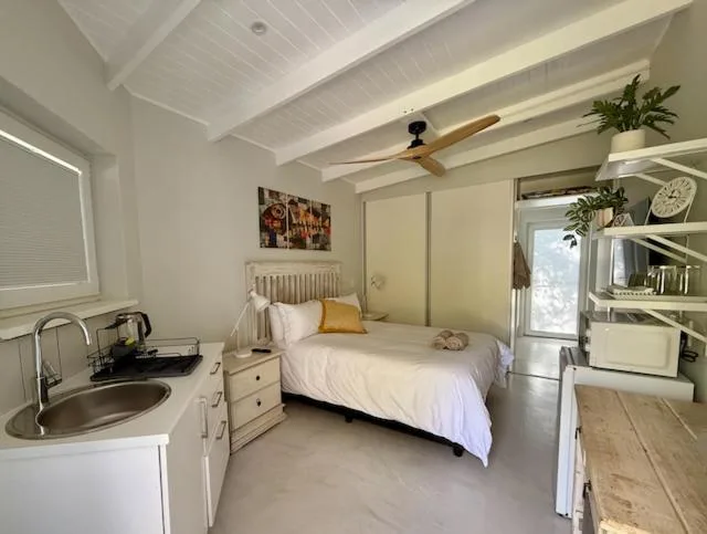 Bright bedroom with white bed, kitchenette, and ceiling fan