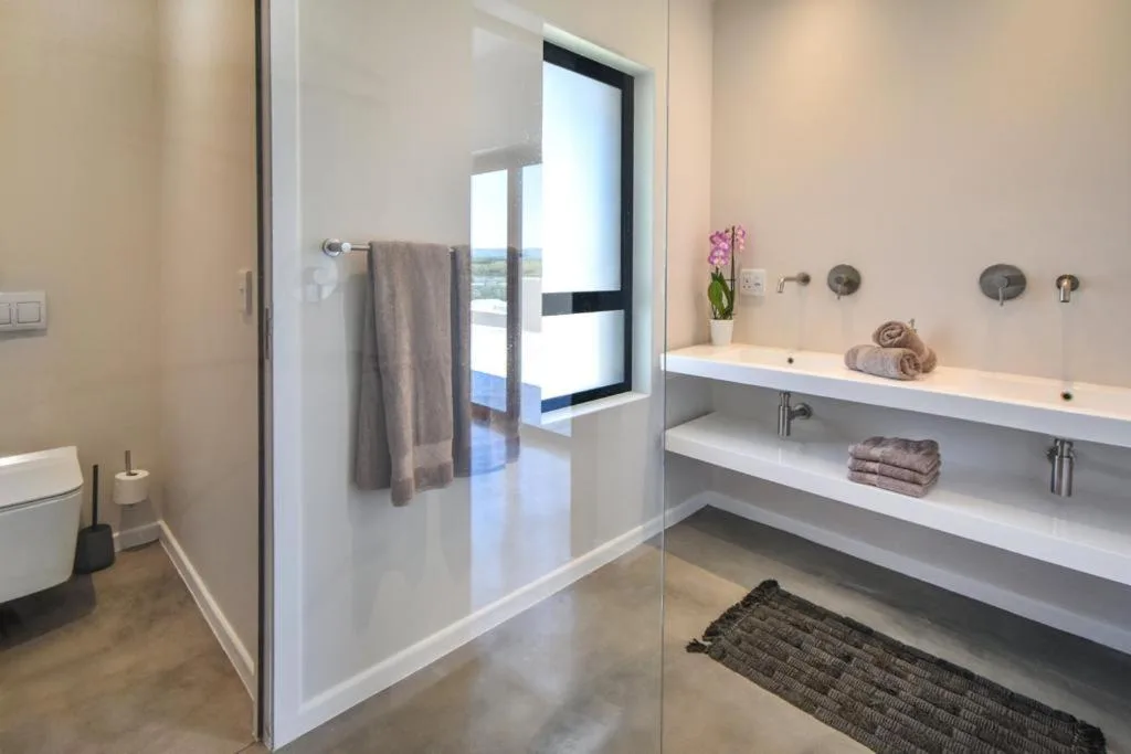 Modern bathroom with walk-in shower, dual vanity, and ocean view window