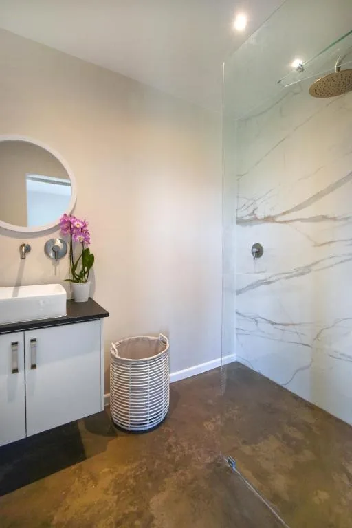 Modern bathroom with marble shower, round mirror, white vanity, and potted orchid