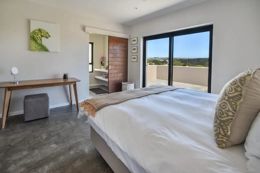 Bright bedroom with queen bed, desk, and glass doors opening to garden views