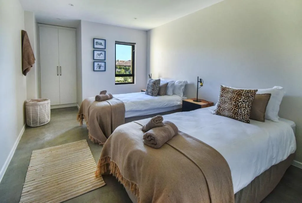 Twin bedroom with white beds, leopard print pillows, and garden view window