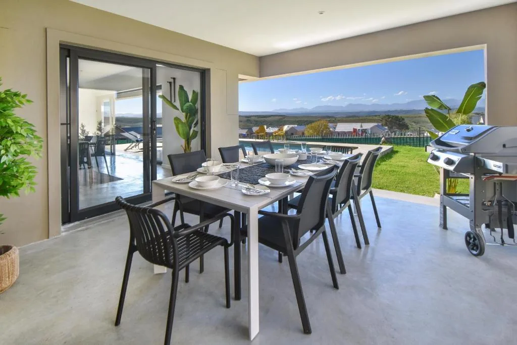 Outdoor dining area with table, chairs, and built-in braai overlooking garden