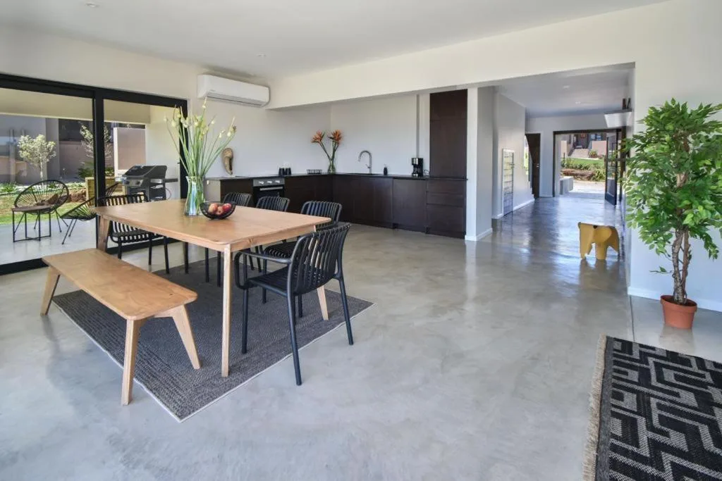 Modern dining area with wooden table, black chairs, and open kitchen beyond