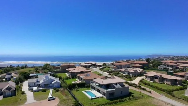 Aerial view of coastal suburb with ocean, mountains, and properties visible