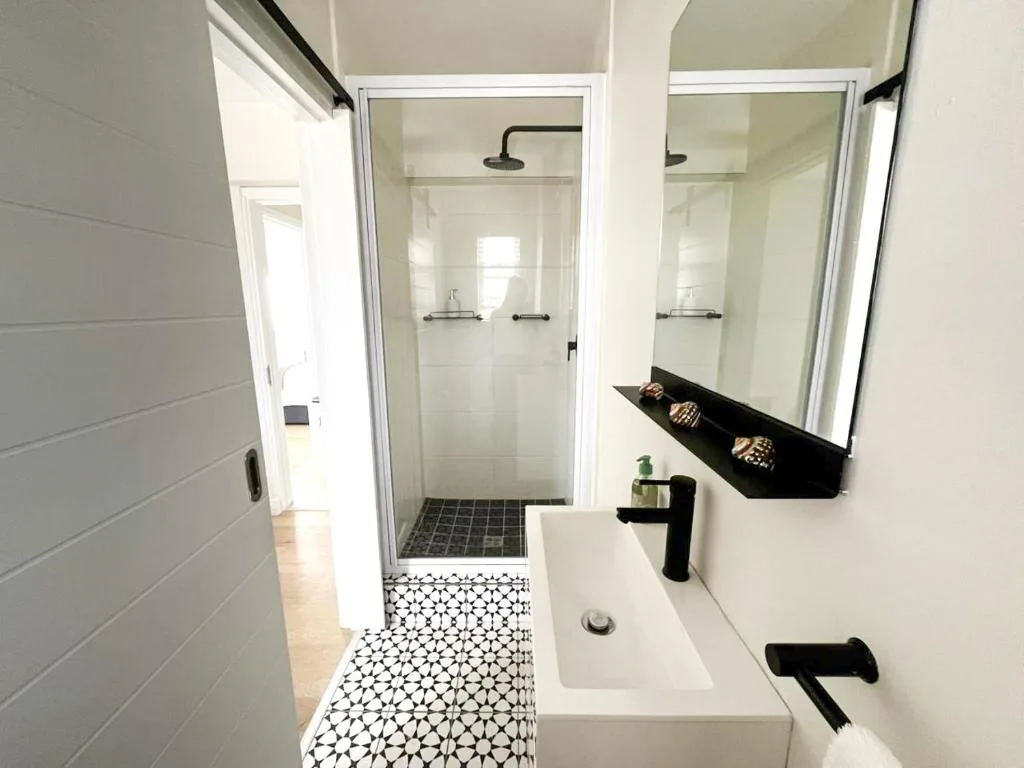 Modern bathroom with walk-in shower, white vanity, black fixtures, geometric floor tiles
