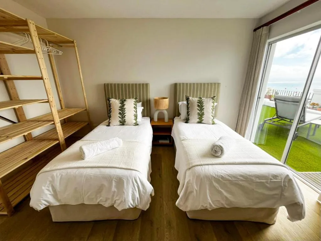 Twin bedroom with white bedding, green patterned pillows, ocean view through glass doors