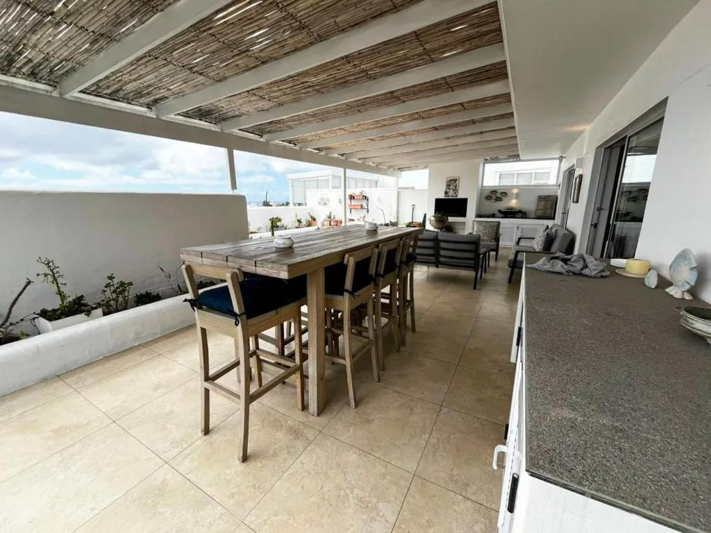 Covered rooftop terrace with dining table, lounge seating, and coastal views