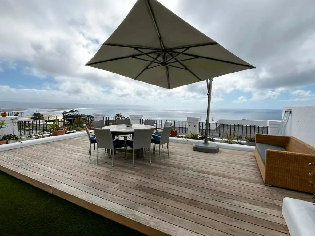 Expansive wooden deck with dining table, umbrella, and ocean views