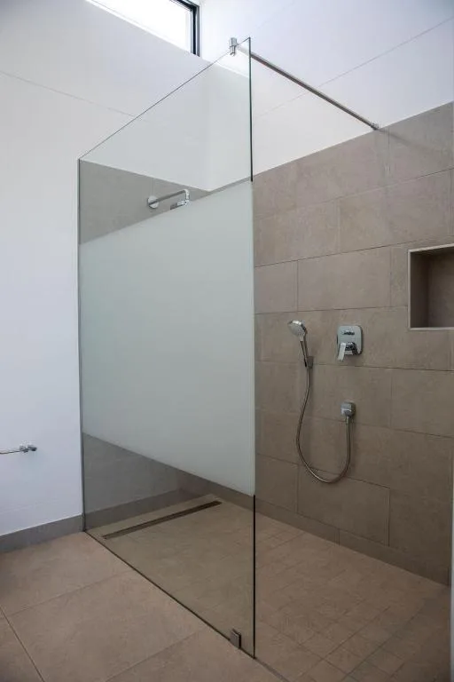 Modern walk-in shower with frameless glass enclosure and beige tile walls