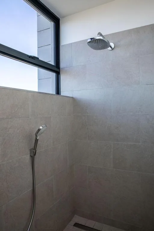 Modern shower with rainfall showerhead and handheld spray against grey tiles