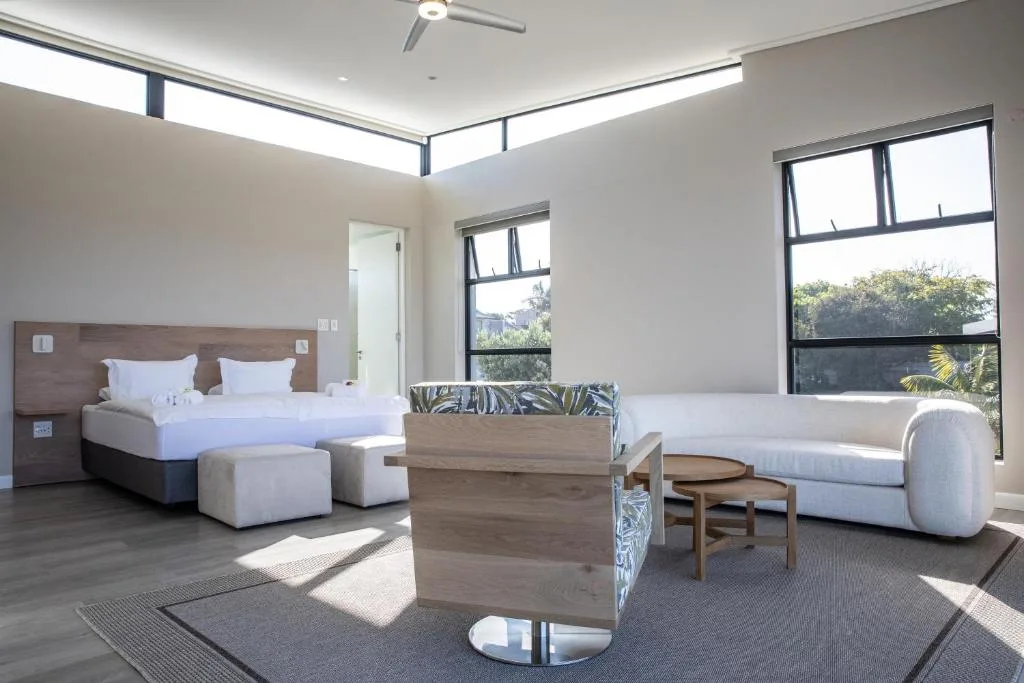 Modern bedroom with queen bed, lounge seating, and expansive windows overlooking gardens