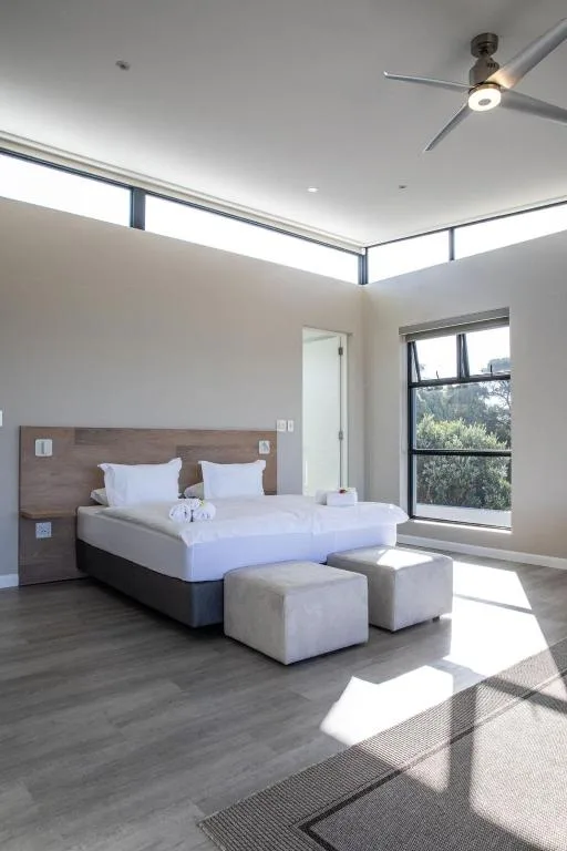 Bright modern bedroom with queen bed, wooden headboard, and garden views