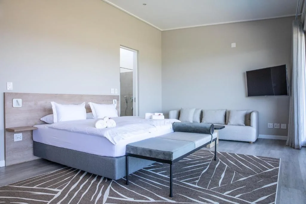 Modern bedroom with king bed, sofa seating area, and wall-mounted TV