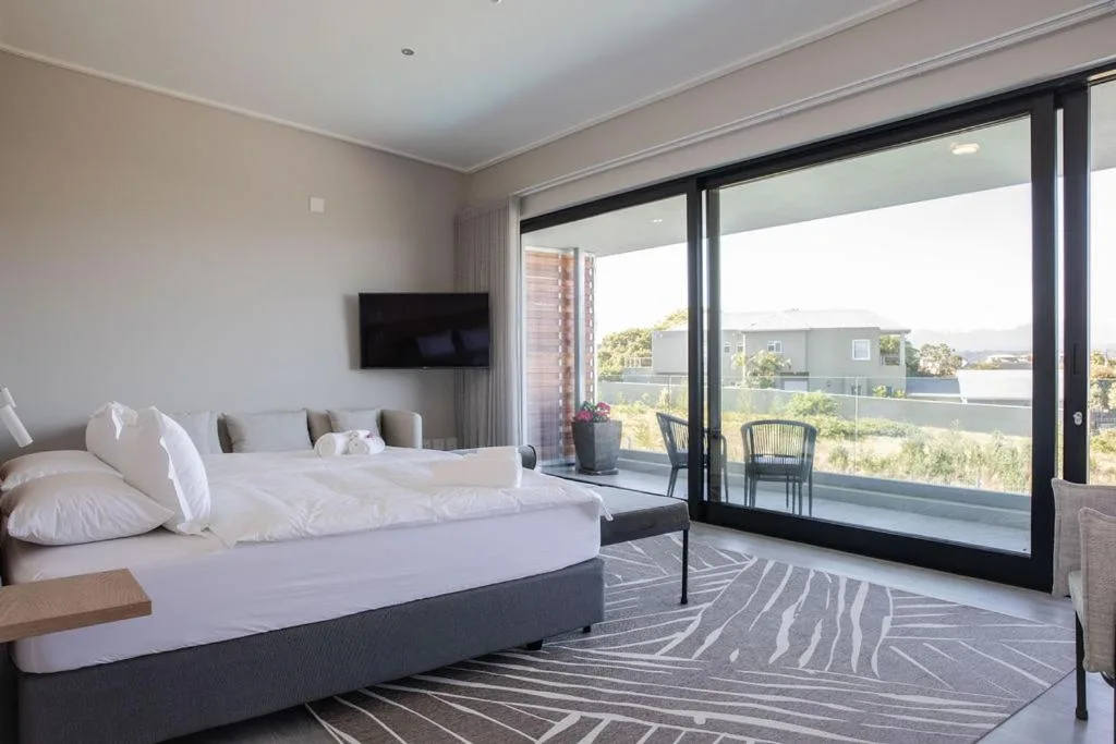 Modern bedroom with king bed and views over Plettenberg Bay landscape through large windows