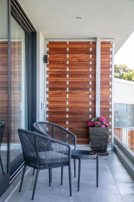 Modern balcony with wooden privacy screen, black chair, and potted flowers