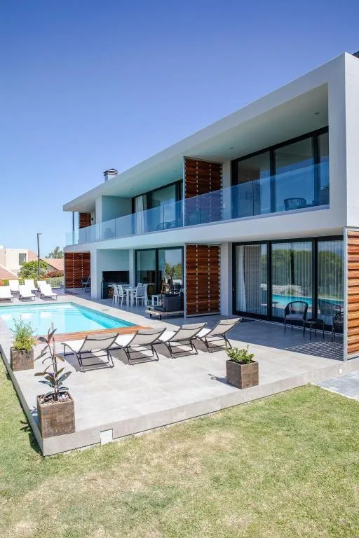 Modern two-story white house with pool, deck chairs, and manicured lawn