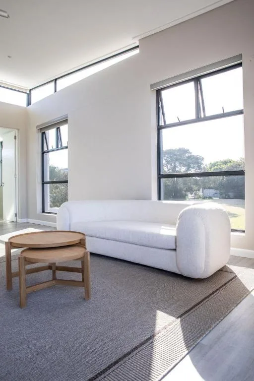 Modern living room with curved white sofa and wooden side tables overlooking greenery