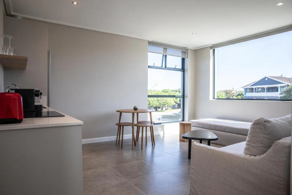 Modern open-plan lounge with sofa, dining table, and large windows overlooking lagoon