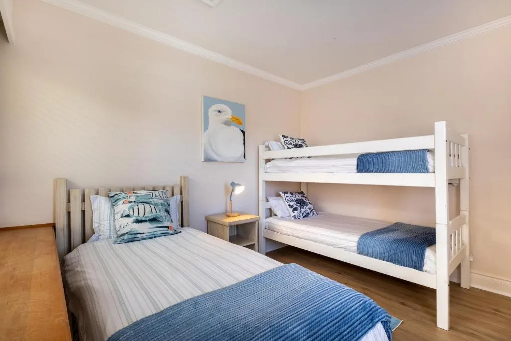 Bright bedroom with single bed and white bunk beds, coastal-themed decor