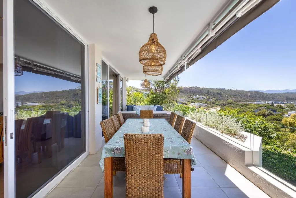 Covered outdoor dining area with woven chairs overlooking lush valley and mountains