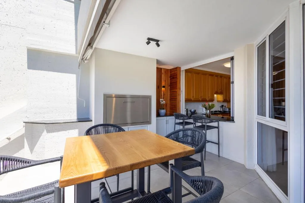 Outdoor patio with wooden dining table and black chairs, kitchen visible through open doors