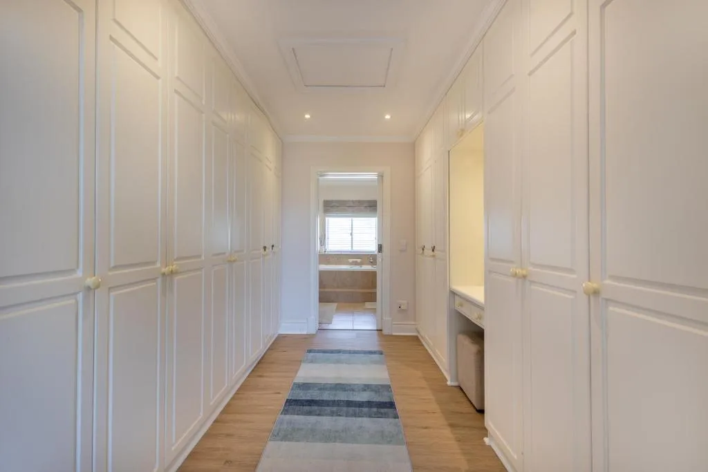 Bright hallway with white cabinetry and wooden floors leading to bedroom