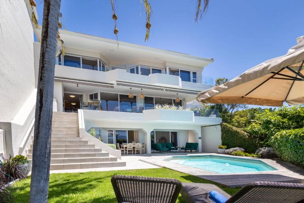 Modern white villa with pool, deck seating, and manicured gardens
