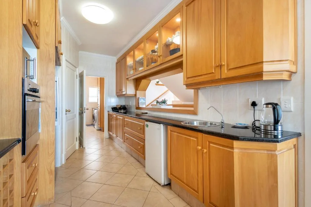 Galley kitchen with wooden cabinetry, black countertops, and stainless steel sink