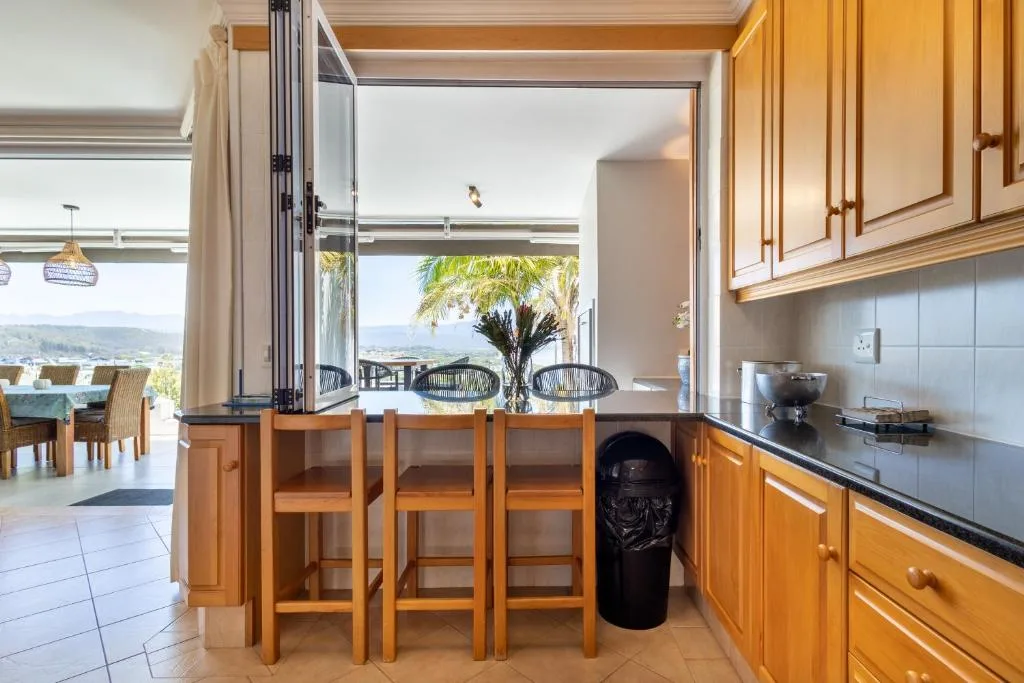 Modern kitchen with wooden cabinetry, island seating, and scenic mountain views through open doors