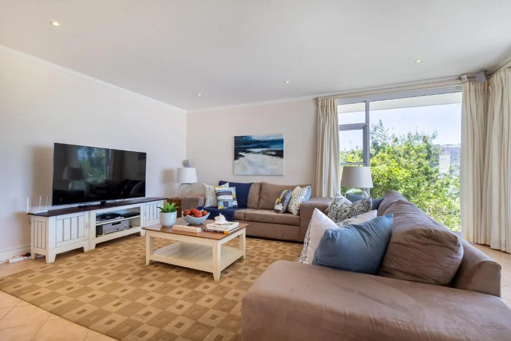 Spacious lounge with tan sofas, TV, and garden views through large windows