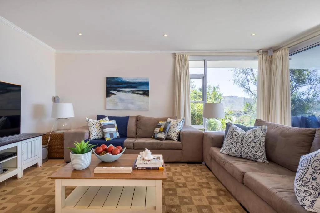 Spacious living room with beige sofas, wooden coffee table, and large windows overlooking gardens
