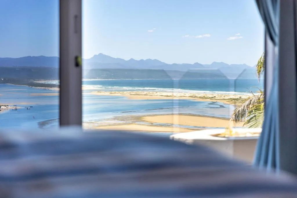 Panoramic ocean and beach vista framed through open window with mountains