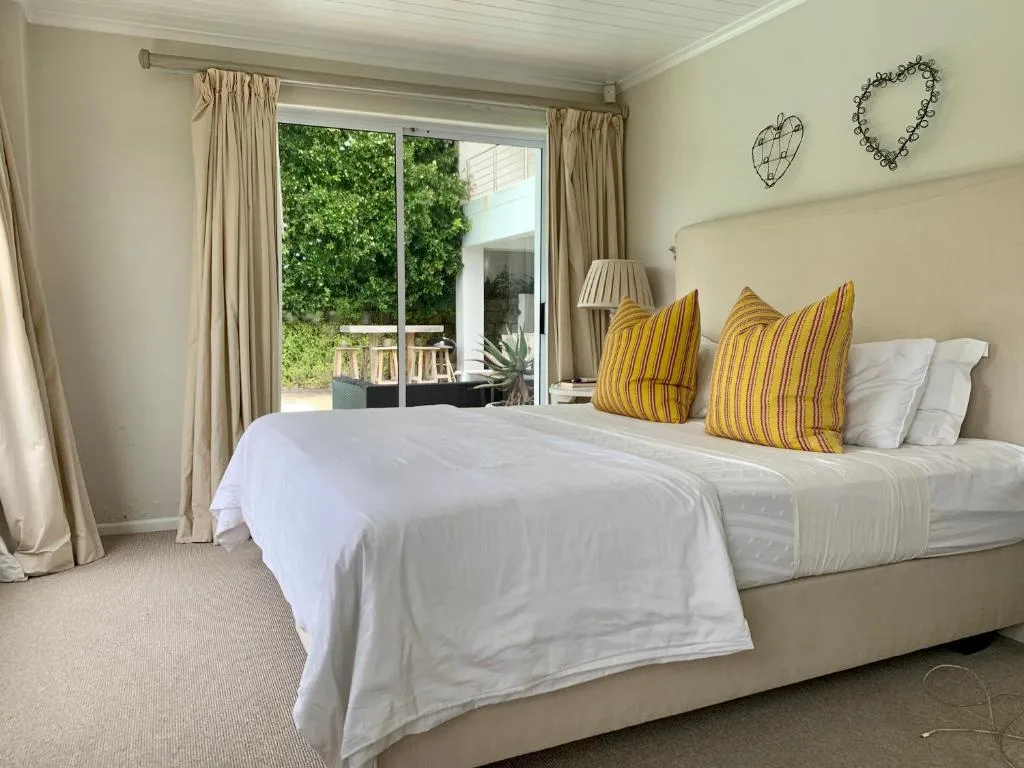 Bright bedroom with twin beds, yellow striped pillows, and glass doors opening to garden deck