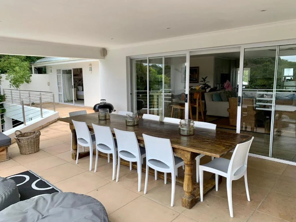 Spacious outdoor deck with wooden dining table and white chairs overlooking garden