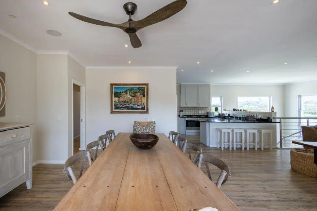 Open-plan dining area with long wooden table and grey chairs, kitchen visible behind