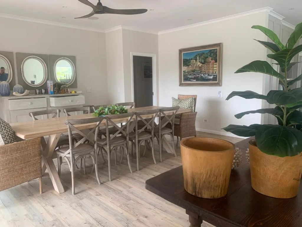 Spacious dining area with wooden table and cross-back chairs, coastal artwork, plants