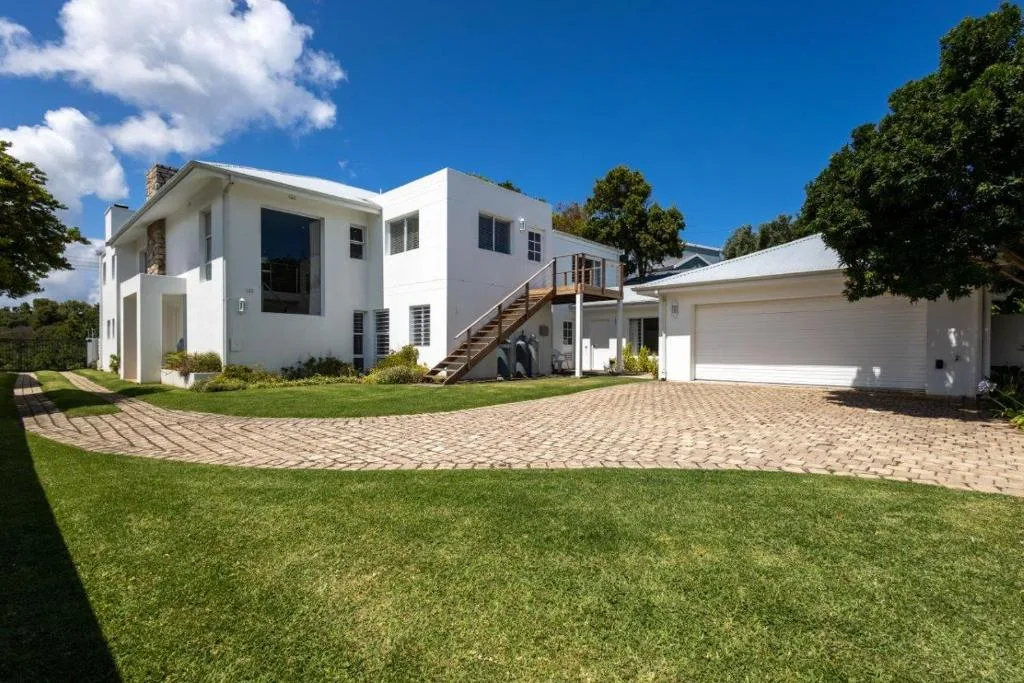 Modern white house with manicured lawn and brick driveway in sunlight