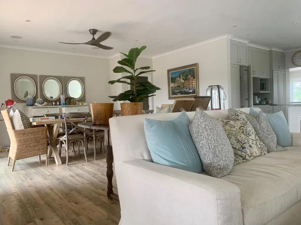 Open-plan lounge with cream sofa, decorative pillows, dining area, and coastal artwork