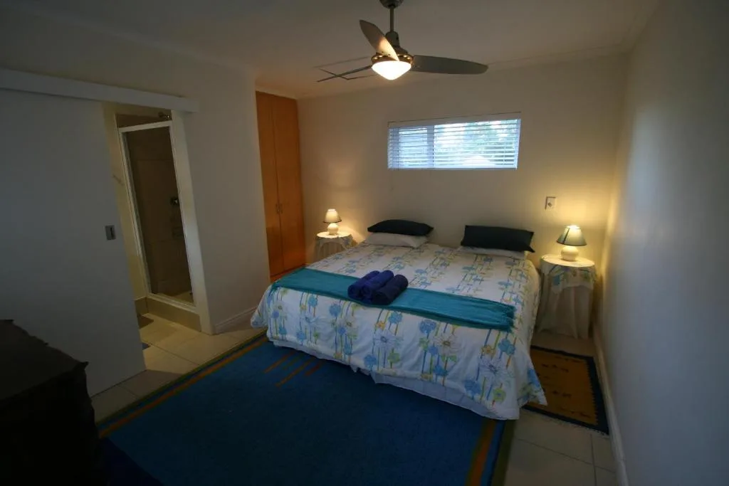 Bright bedroom with queen bed, bedside lamps, ceiling fan, and window light