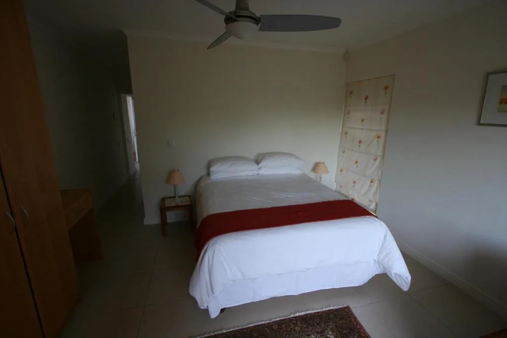 Spacious bedroom with double bed, white linens, red runner, and ceiling fan