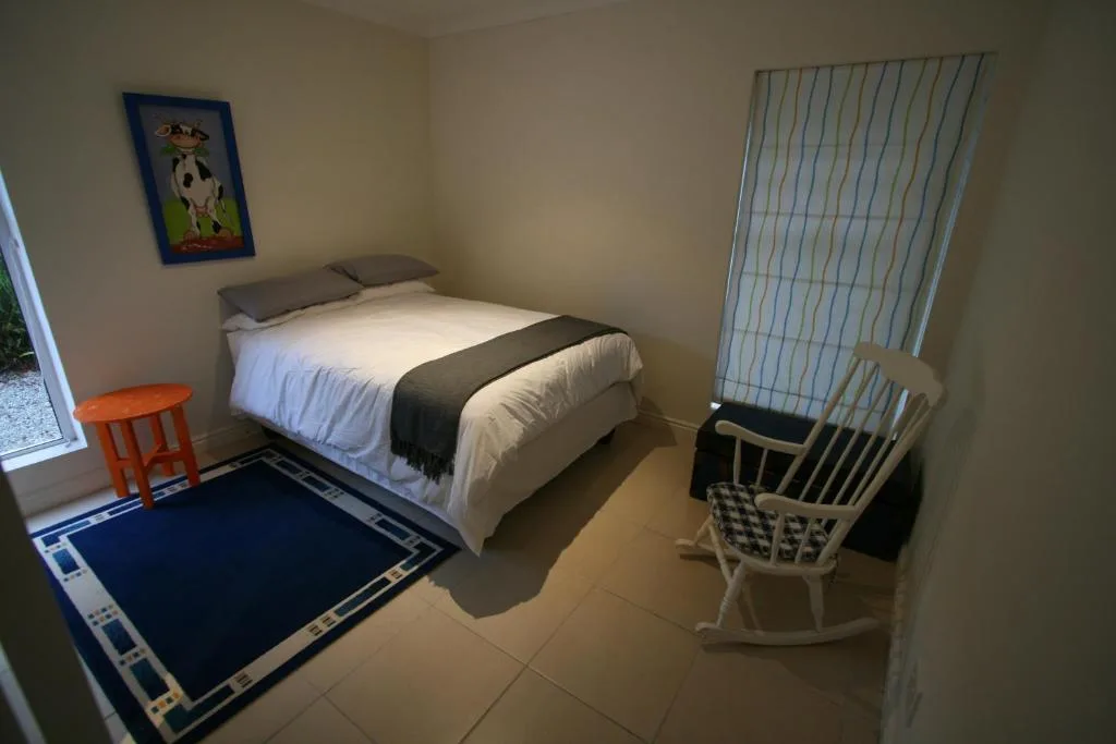 Bright bedroom with queen bed, blue rug, rocking chair, and garden view