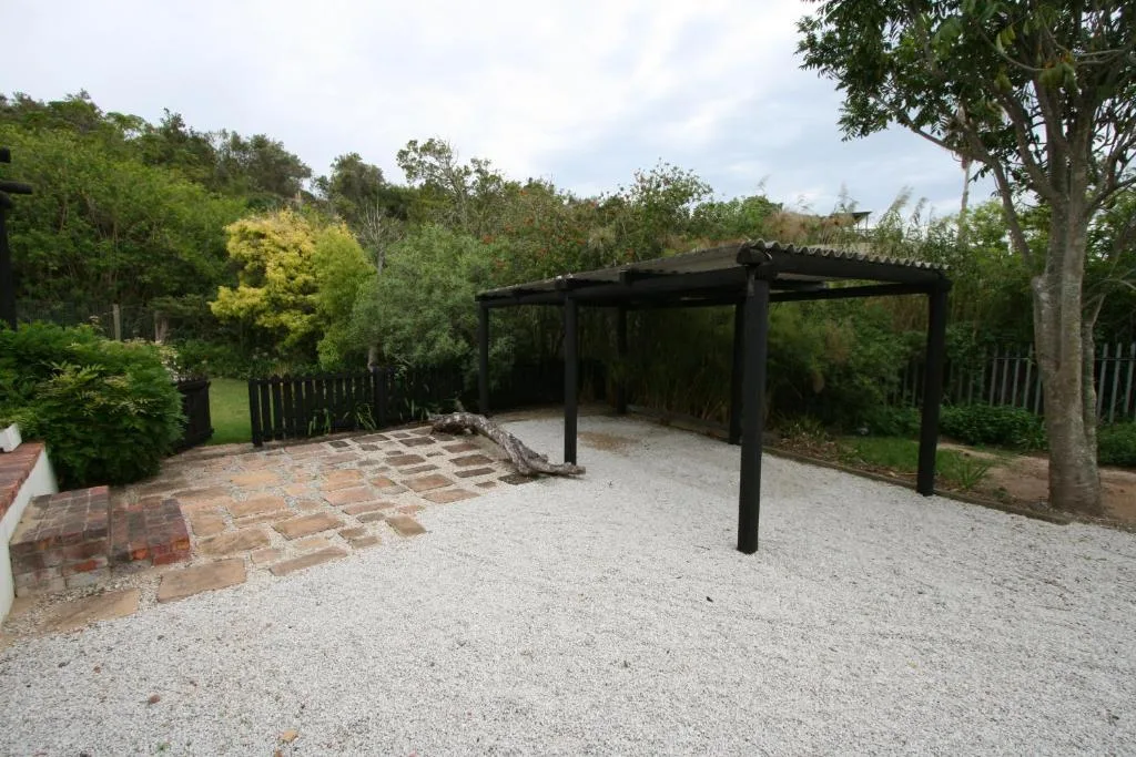 Spacious outdoor patio with black pergola and gravel surface surrounded by gardens